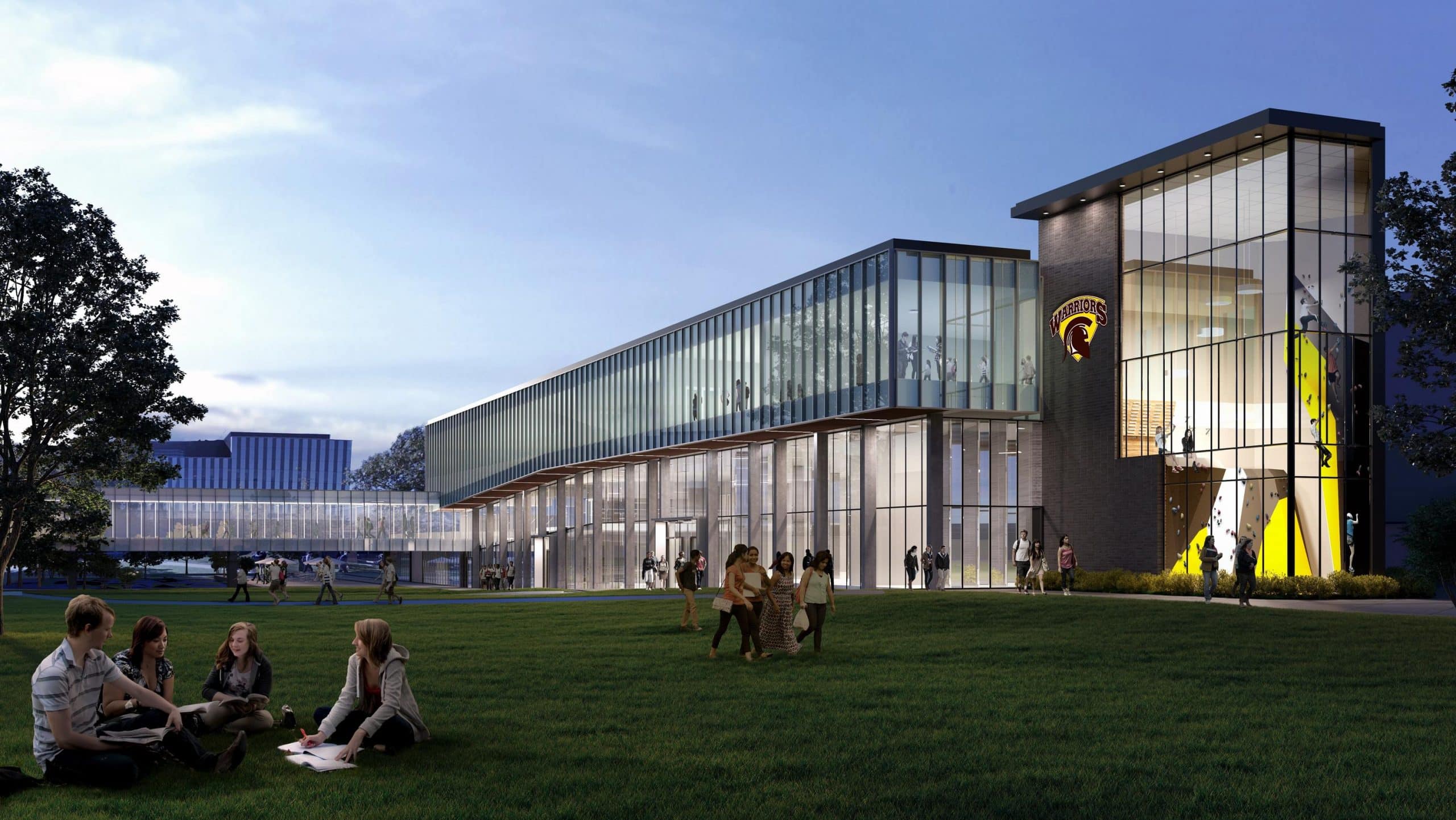 A modern glass and brick building with people sitting and walking on a green lawn in front, featuring a university logo on the building.