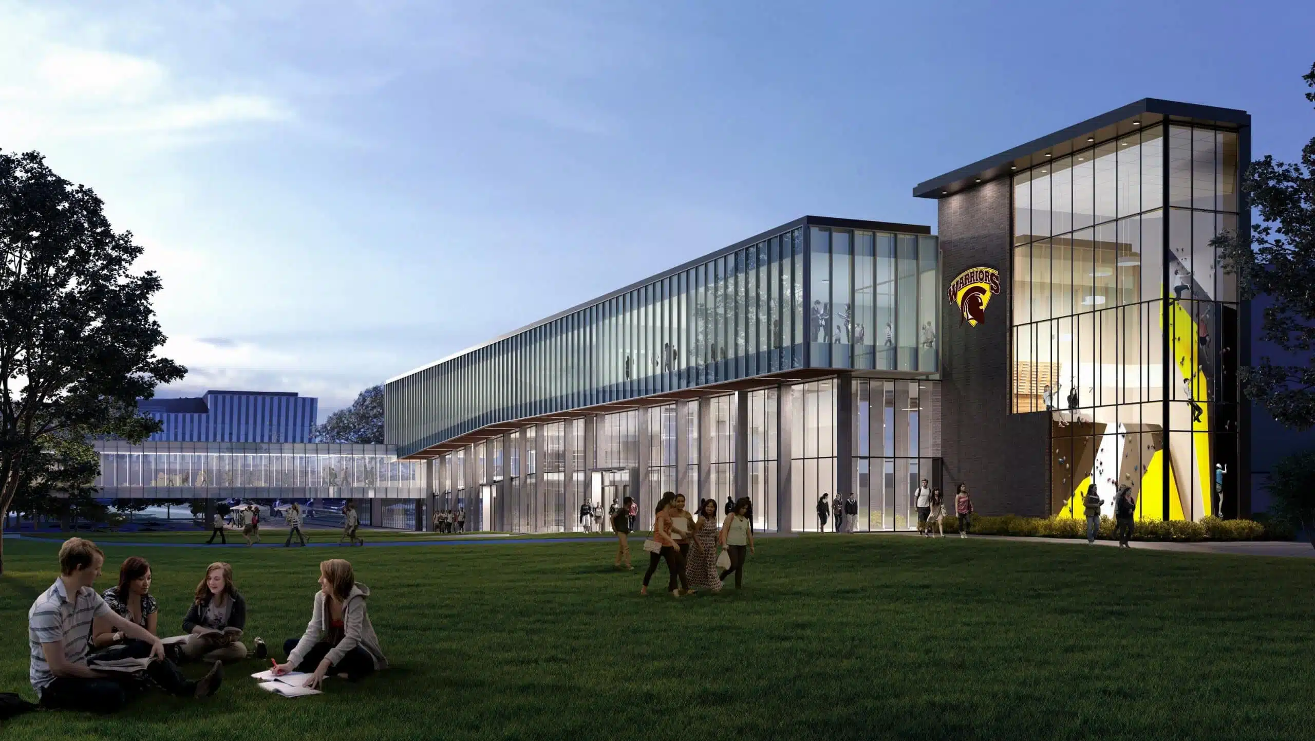 A modern glass and brick building with people sitting and walking on a green lawn in front, featuring a university logo on the building.