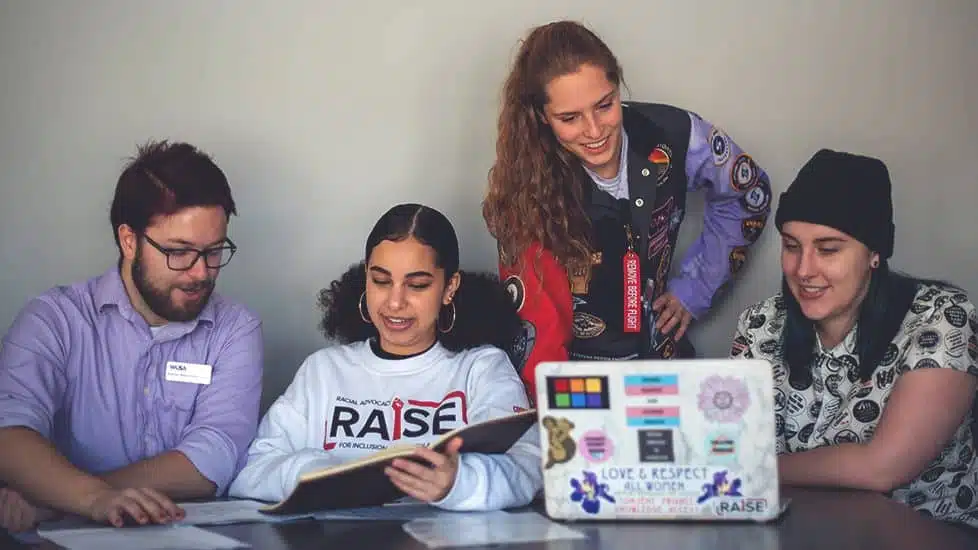 Four people are gathered around a table, looking at documents and a laptop, engaging in a discussion about advocacy.