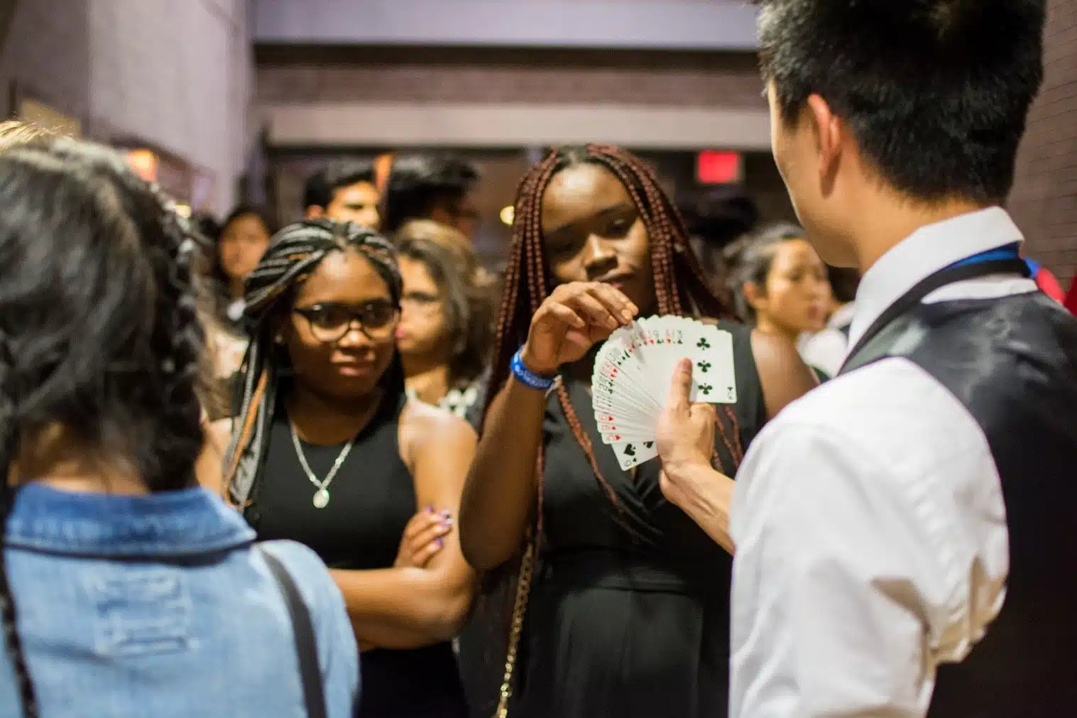 A group of people watches as a man in a black vest and white shirt performs a card trick, bringing unexpected entertainment to the general meeting.