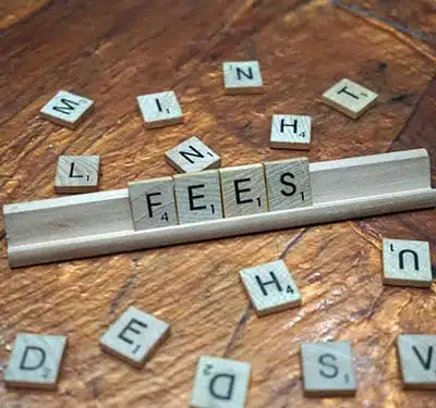 Scrabble tiles on a wooden surface, arranged to spell "FEES" on a tile rack, with additional scattered tiles showing random letters—a nod to the general rules of wordplay and strategy.