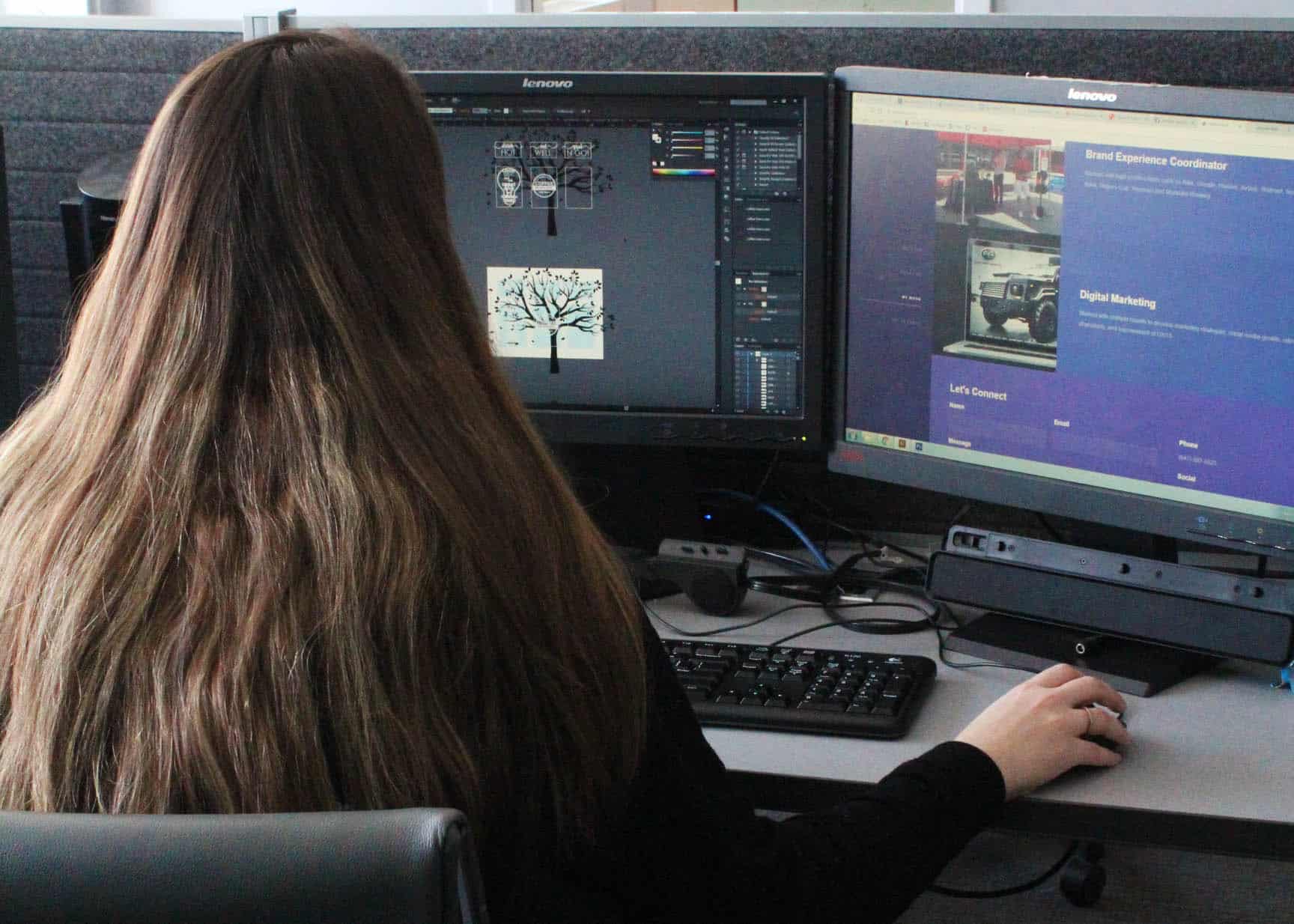 A person with long hair sits at a desk, working on graphic design software on a computer with dual monitors, while referencing General Meeting Rules.