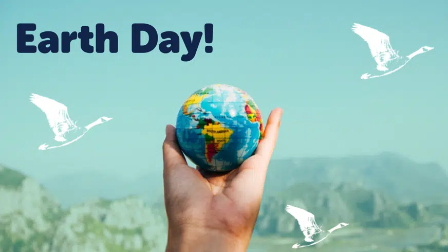 A hand holding a small earth globe against a mountainous backdrop with "Earth Day!" text and white birds in the sky flying in different directions.