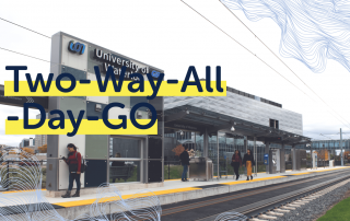 Shot of a train station platform with a modern building in the background. The text "Two-Way-All-Day-GO" is prominently displayed. Passengers, including students who benefit from the reliable GO Train Service, are waiting on the platform, and rail tracks are visible.