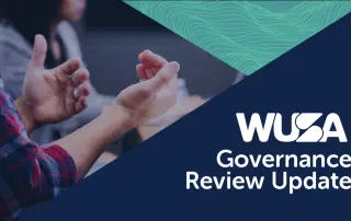 Two individuals are engaged in discussion at a table, with text in the foreground that reads "WUSA Governance Review Update - February 2022" on a blue and green background.