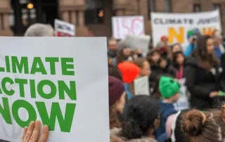 A group of people holding signs at a UW Climate Emergency protest, with a prominent sign in the foreground reading "CLIMATE ACTION NOW.