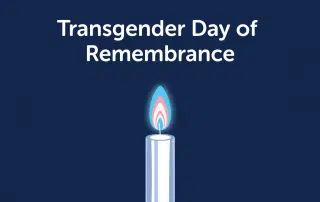 A candle with a flame in the colors of the transgender pride flag on a dark blue background. Text above reads "Transgender Day of Remembrance 2021.