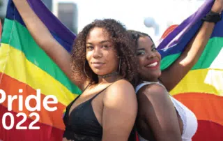 Two people smile while holding up a rainbow flag at a Pride event, embodying the theme "Finding Your Community." Text on the image reads "Pride 2022.