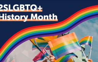 A vibrant graphic features "2SLGBTQ+ History Month 2022" in bold white text against a dark blue background. Below the text, multiple hands wave rainbow flags in the air. A sweeping rainbow stripe arcs across the middle of the image, adding to the celebratory atmosphere.