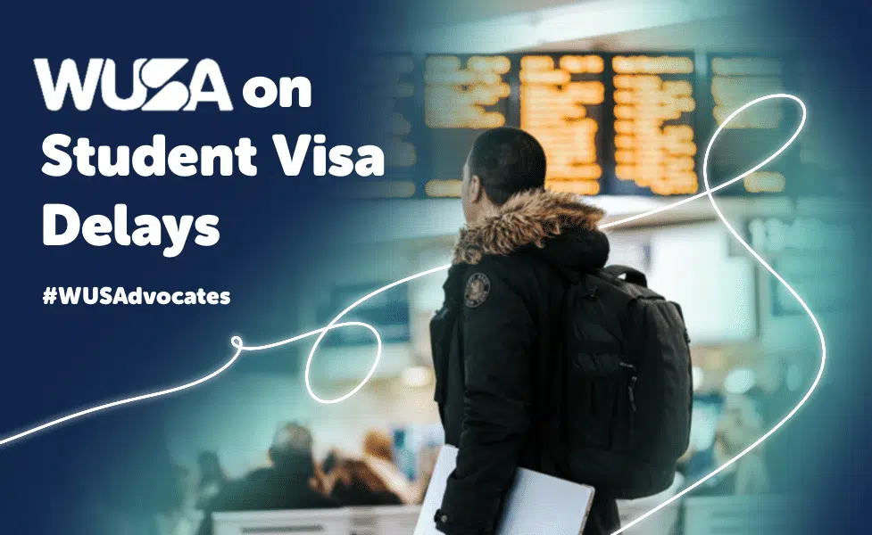 A person in a jacket with a backpack looks at an information board in a busy terminal. The text reads "WUSA on Student Visa Delays #WUSAdvocates". White lines add decorative elements across the image.