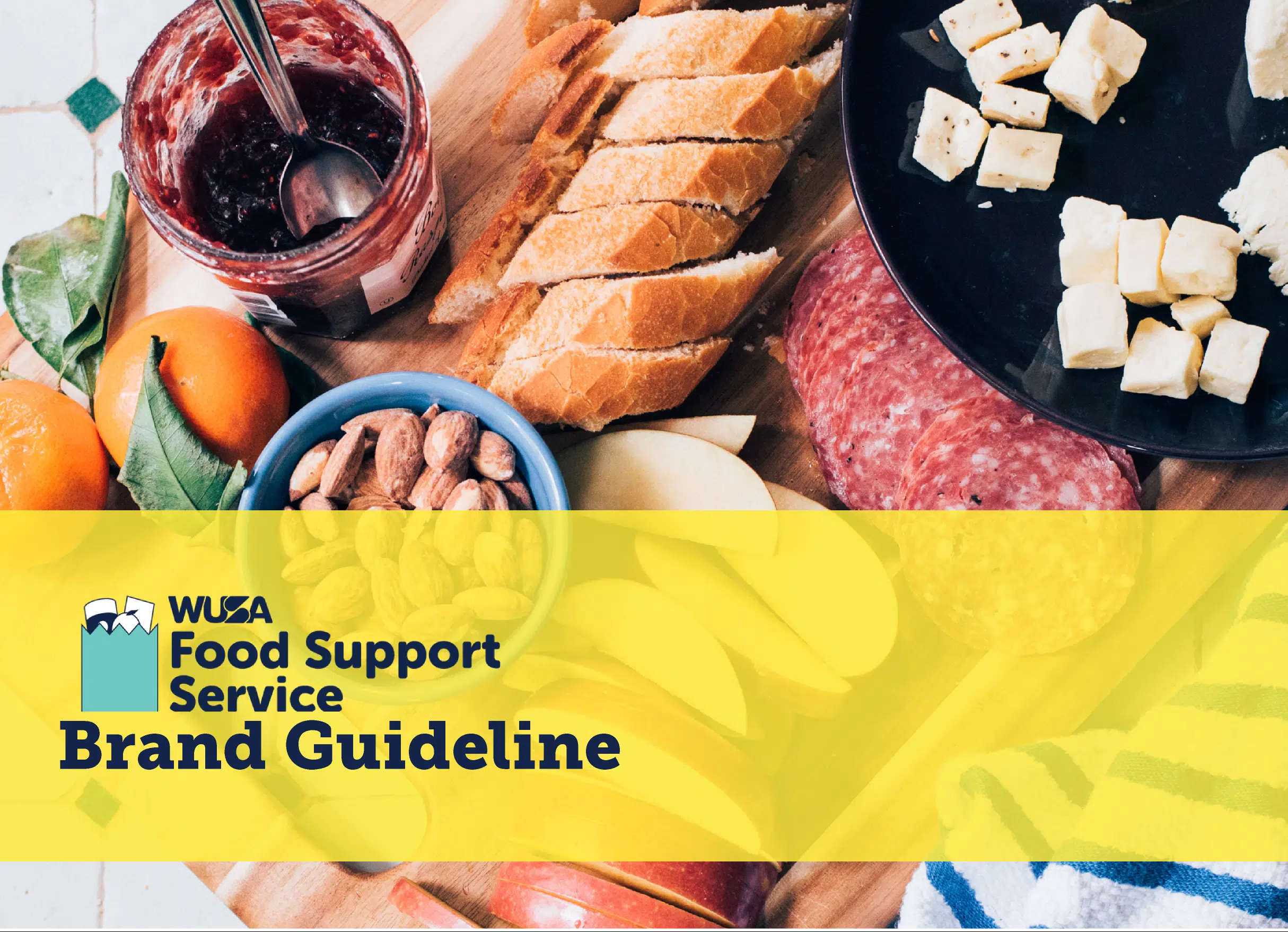 An assortment of food items including bread, cheese, sliced meats, and fruit is displayed on a wooden board. In the foreground, a yellow banner with the WUSA Food Support Service logo and the text "Brand Guideline" is visible.