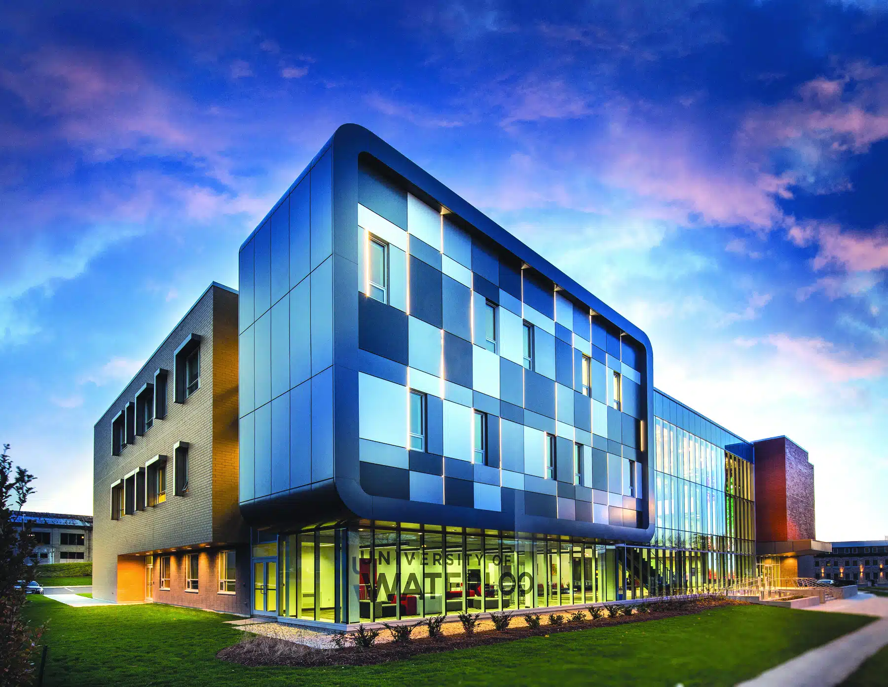 Modern, multi-story building with a striking design, featuring a mix of blue and green glass panels and large windows. The structure is part of an educational institution with the name "Université de l'Ontario français" visible on the lower part of the building. The sky is pink and blue at sunset, setting the stage for the launch of their innovative GBDA Pilot Bus Program.