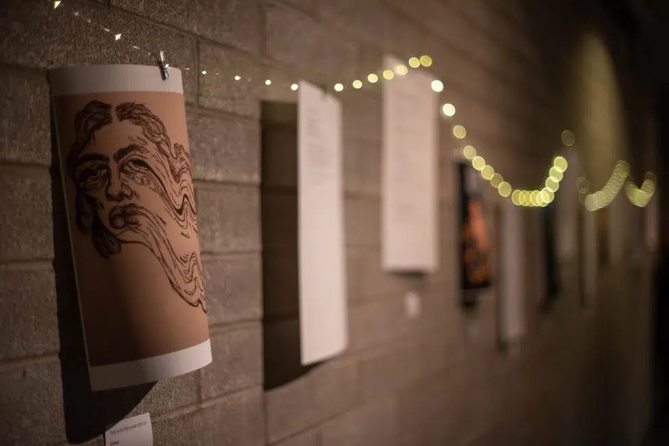 Image of a collection of printed imagery and poems hung up on a wall using string lights.
