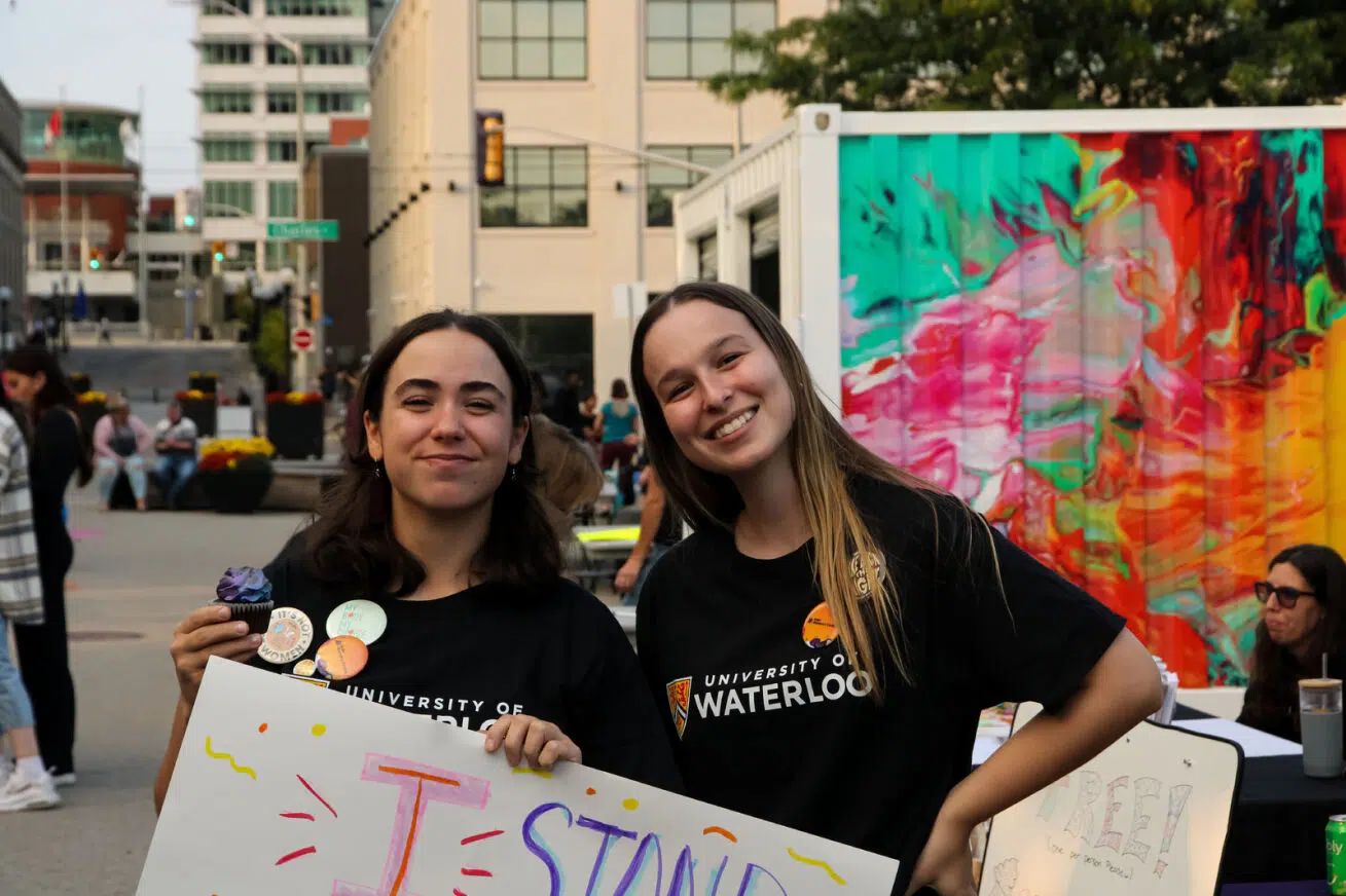 Two female-presenting students in University of Waterloo shirts posing together with a march sign.