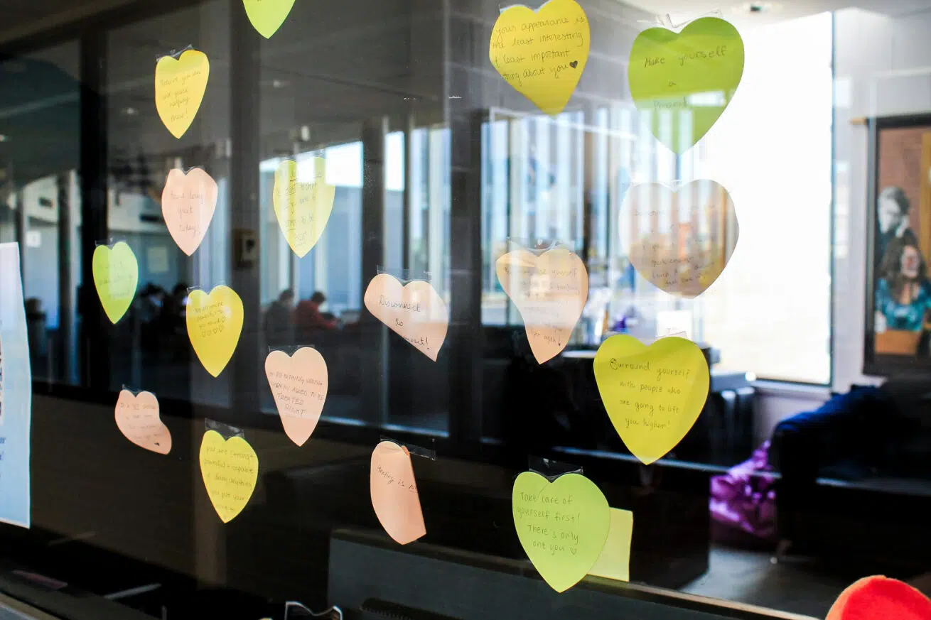 Image of sticky notes shaped like hearts with positive and empowering messages on the window of the Women's Centre.