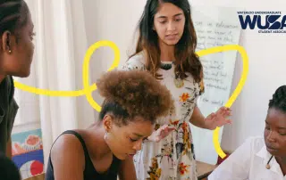 A group of students are engaged in a discussion around a table. A female student stands, explaining something to three seated students who are listening attentively. The Waterloo Undergraduate Student Association logo is visible in the corner of the image.