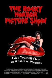 Poster for "The Rocky Horror Picture Show" featuring a person wearing a corset and fishnet stockings, lounging on a large red lips couch. The title is in bold, dripping red letters at the top. Perfect for Halloween activities in the KW Region, with text at the bottom reading "Give yourself over to absolute pleasure.