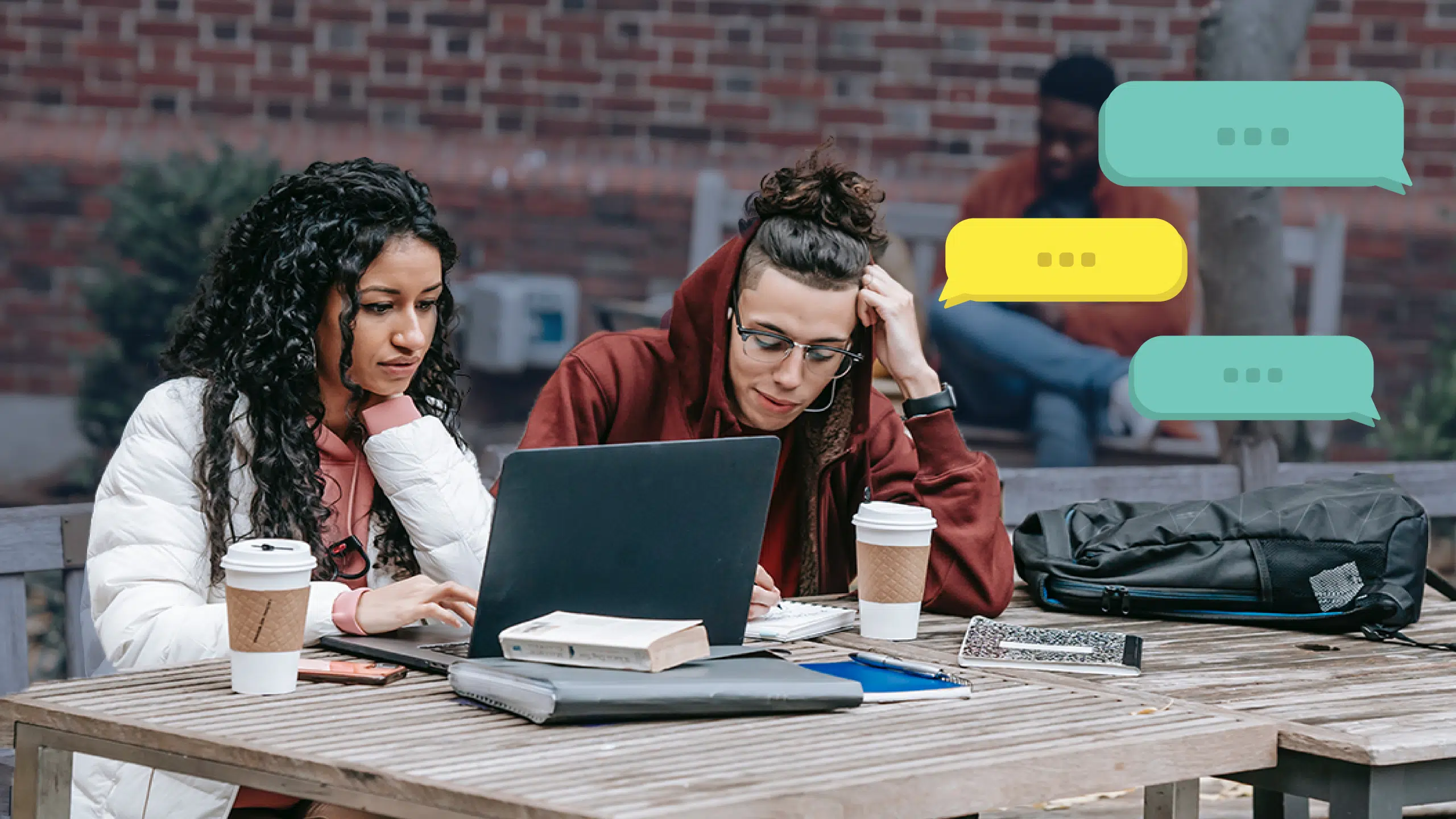 Two individuals sit at a wooden table outdoors, focused on a laptop during an OUSA consultation. Both appear engaged in their work, surrounded by books and coffee cups. Three chat bubbles hover near the image, indicating a conversation. A brick wall and another person are visible in the background.