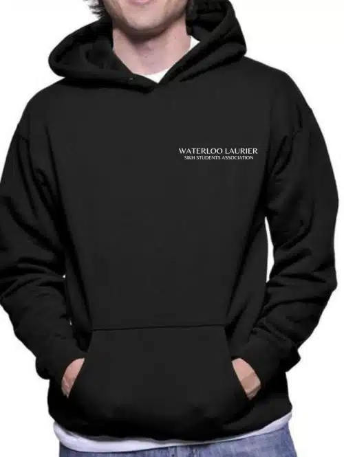 A person is wearing a black Sikh Student Association (SSA) Hoodie with their hands in the front pocket. The hoodie has the text "WATERLOO LAURIER SINO STUDENTS ASSOCIATION" written on the upper left side. The person is smiling and standing against a plain background, proudly representing their SSA spirit.