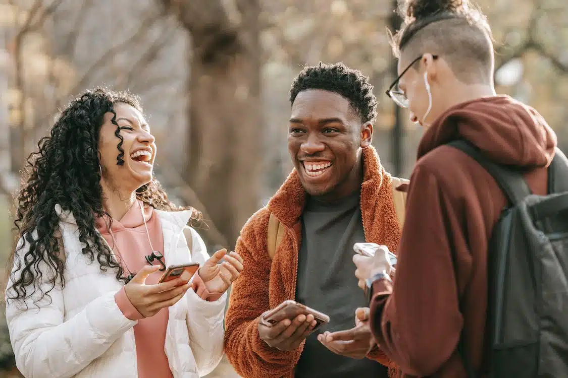 Three students laughing while holding coffee in the chilly weather.