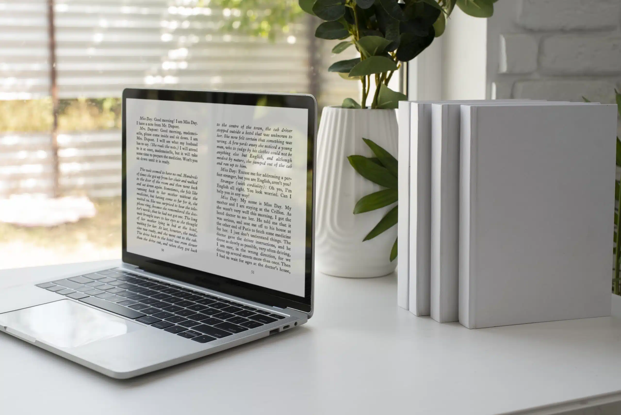 A laptop displaying text from an open e-book is placed on a white desk, promoting ways to save money on books. Next to the laptop are three blank white books stacked upright. A potted plant is in the background near a window with blinds, casting gentle natural light into the room.