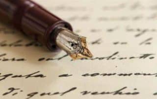 A close-up image of a vintage fountain pen with a metal nib resting on a piece of handwritten verse. The handwritten text is blurred, making it unreadable, while the details of the pen and its nib are in sharp focus.
