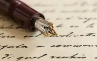 A close-up image of a vintage fountain pen with a metal nib resting on a piece of handwritten verse. The handwritten text is blurred, making it unreadable, while the details of the pen and its nib are in sharp focus.