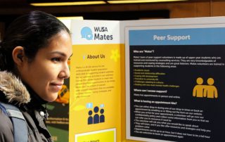 A person in a winter coat reads an informational display about "Peer Support" offered by "MUSA Mates." The display includes sections titled "About Us" and "Who are Mates?" with text explaining their roles and support services, which can be especially helpful during exam season.