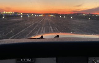 View from inside a cockpit of a small aircraft during taxiing or takeoff at an airport runway. The runway lights are illuminated, and the sky displays a colorful sunset with shades of orange, pink, and purple. Capture your favourite activity to unwind for the April 2024 Photo Contest!