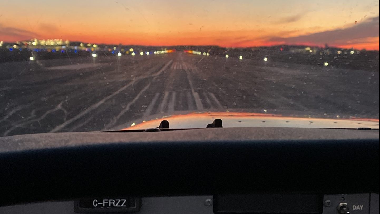 View from inside a cockpit of a small aircraft during taxiing or takeoff at an airport runway. The runway lights are illuminated, and the sky displays a colorful sunset with shades of orange, pink, and purple. Capture your favourite activity to unwind for the April 2024 Photo Contest!