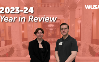 Two individuals stand in front of a grand staircase inside a spacious, elegantly decorated hall with a high ceiling. The title "2023-24 Governance Year in Review" appears on the left, and the letters "WUSA" are in the top right corner.