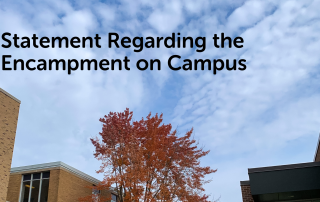 A statement that reads "Statement Regarding the Encampment on Campus" is overlaid on a photo of a partly cloudy sky, with an autumn-colored tree and portions of two brick buildings visible on either side.