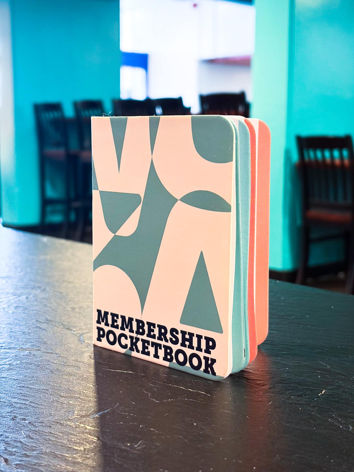 2026-27 Membership Pocketbook A small, colorful WUSA membership pocketbook stands upright on a dark table in a bright room.