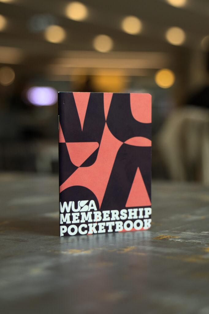 A WUSA Pocketbook stands upright on a table with a blurred background, showcasing the sleek design of this exclusive membership accessory.