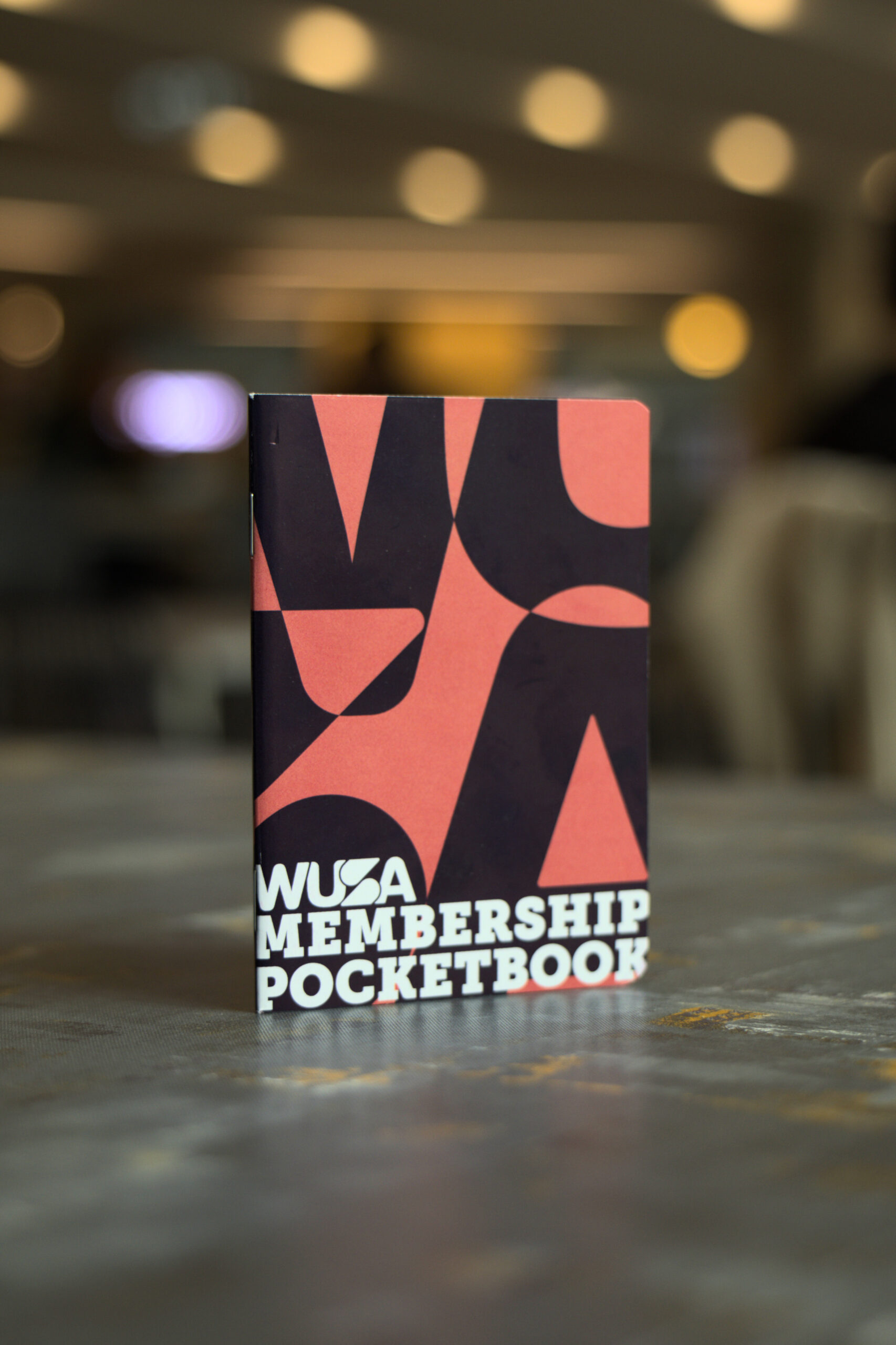 A WUSA Pocketbook stands upright on a table with a blurred background, showcasing the sleek design of this exclusive membership accessory.