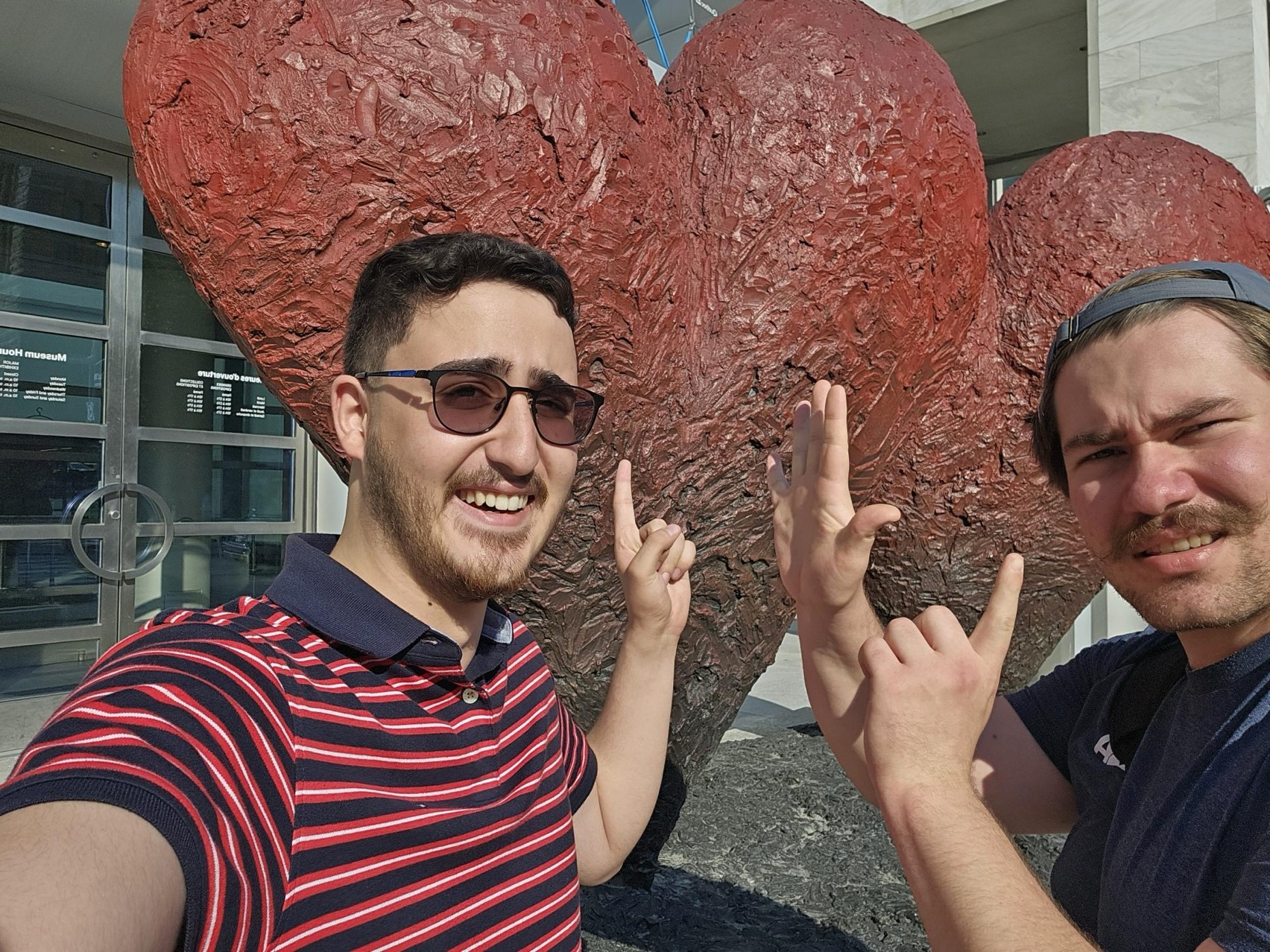 President Nick and VP Arya smiling and pointing to sculptures of red 'hearts' behind them.