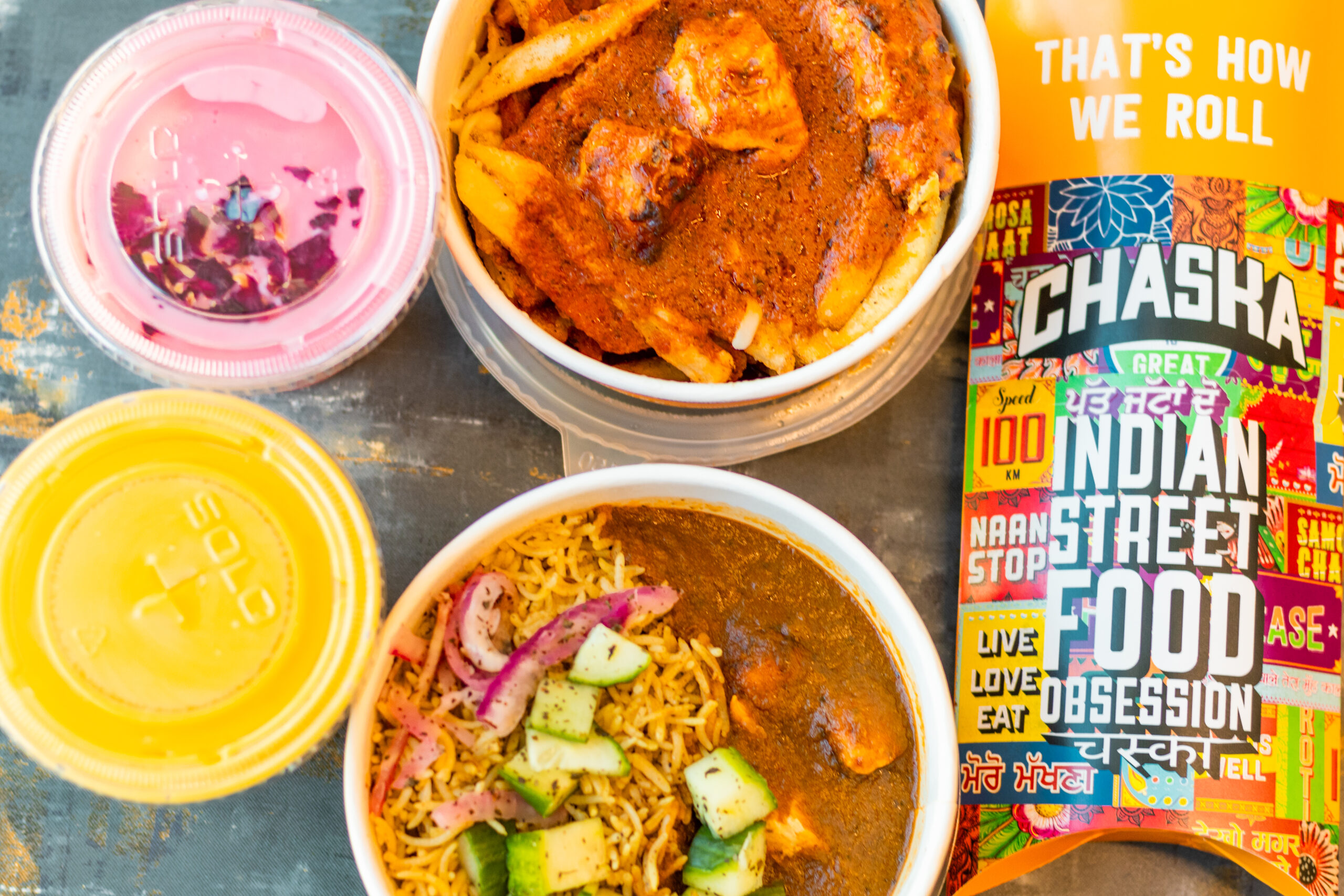 Dive into the vibrant world of Indian street food with a dazzling "Chaska" package, featuring curry, rice, fries, and pink and yellow drinks. This colorful feast is a festival for your taste buds and promises an unforgettable culinary adventure!