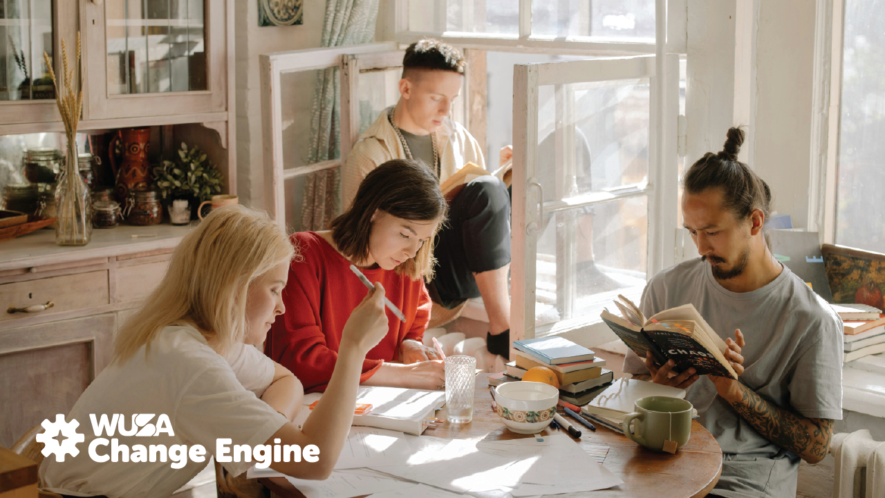 Four people gather around a sunlit table, engrossed in reading and discussing the latest insights from the Change Engine, surrounded by papers and books.