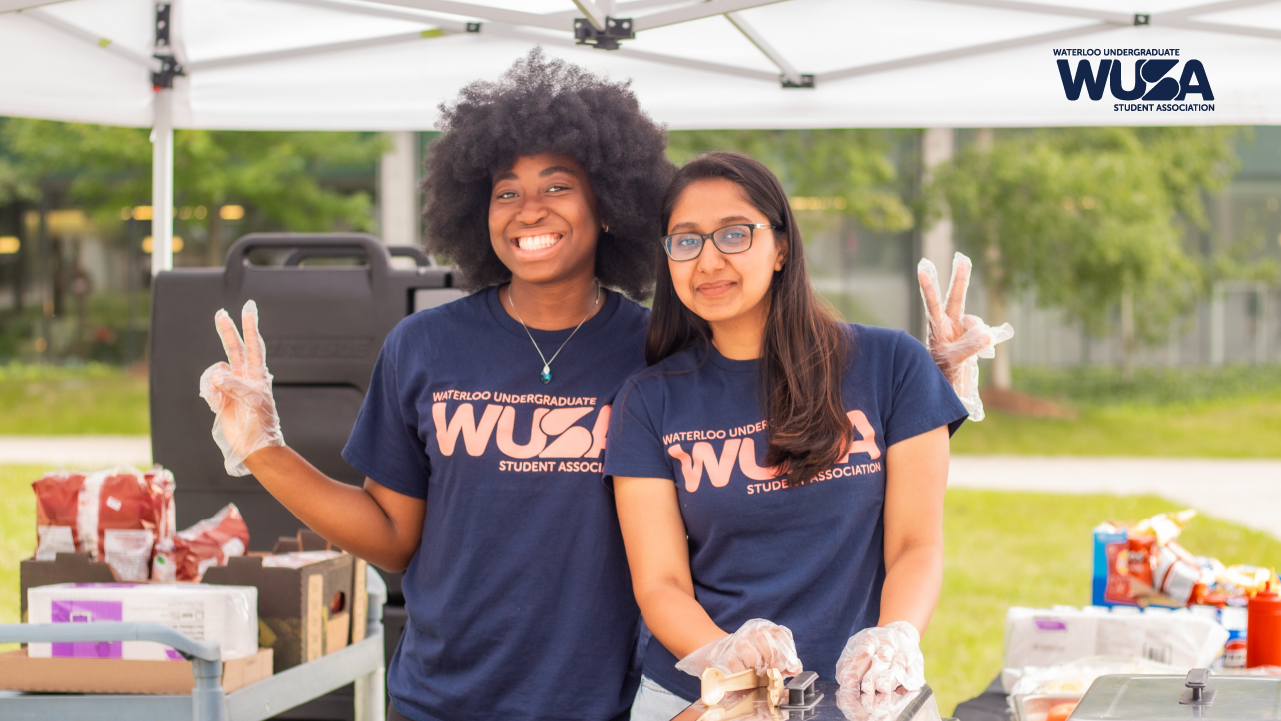 Two smiling people wearing matching T-shirts at an outdoor event, with one holding a peace sign, celebrate their Volunteer Recognition.