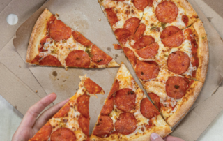 At the pizza party, a person eagerly grabs a slice of pepperoni pizza from the box, ready to pair it with a refreshing glass of soda.