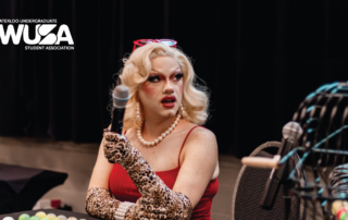 A person in a glamorous outfit holds a microphone at an all-ages event, adorned with the "Waterloo Undergraduate Student Association" logo.