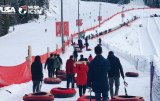 At Chicopee, people in winter clothing walk uphill with snow tubes on a snowy slope, passing by the red safety netting.