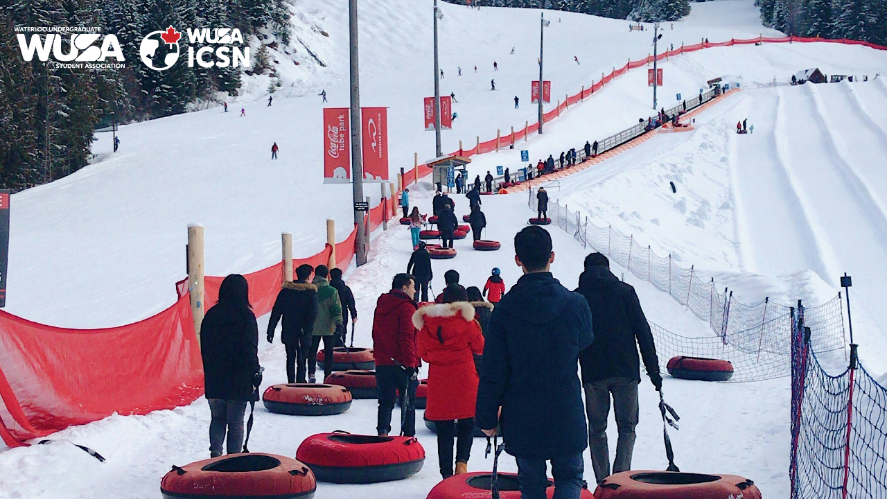 At Chicopee, people in winter clothing walk uphill with snow tubes on a snowy slope, passing by the red safety netting.