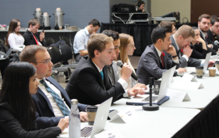 People sitting at a conference table with laptops and microphones engage in discussion, passionately championing student advocacy.