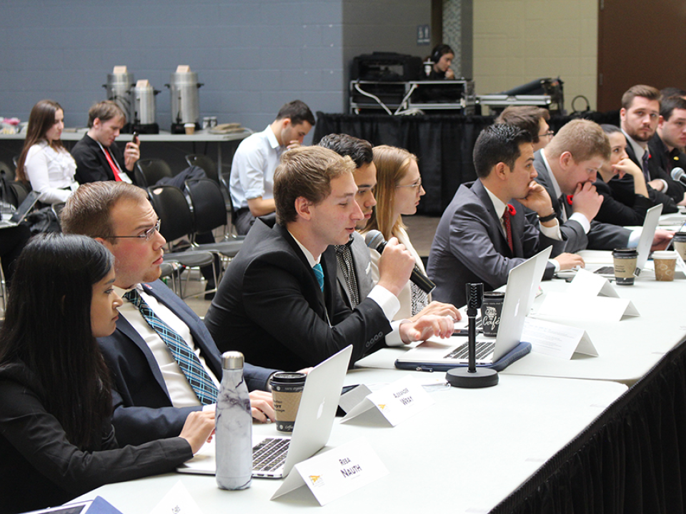 People sitting at a conference table with laptops and microphones engage in discussion, passionately championing student advocacy.