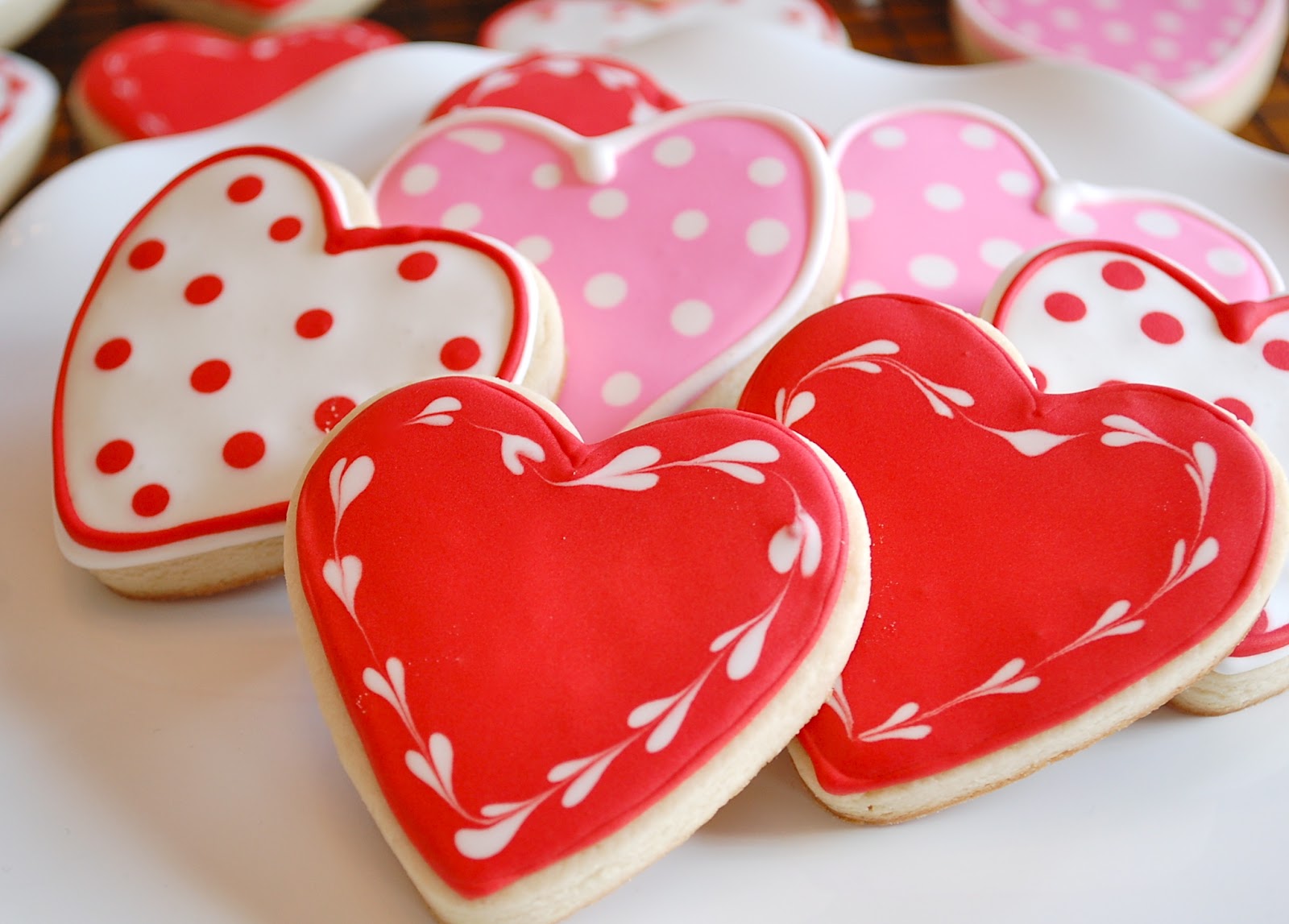 Valentine's heart-shaped cookies with red, pink, and white icing, featuring polka dots and decorative patterns perfect for cookie decorating with mates.