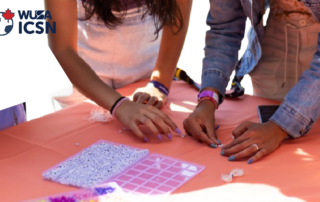 People enjoy a Stress-Free Friday, crafting with beads at a table covered with an orange cloth under the "WUSA ICSN" logo.