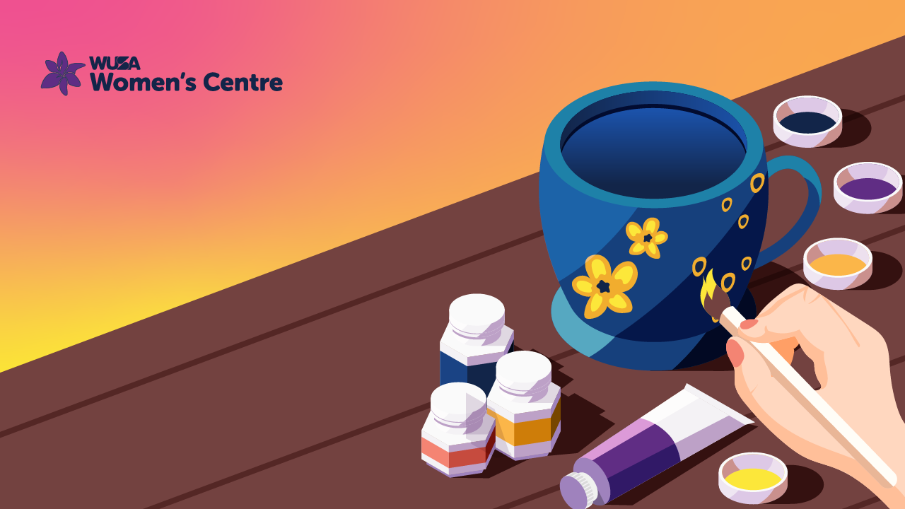 Hand painting a blue mug with flowers, perfect for your morning sip, surrounded by vibrant paints on a wooden surface. The "Women's Centre" logo graces the corner, adding a touch of community spirit to this creative endeavor.