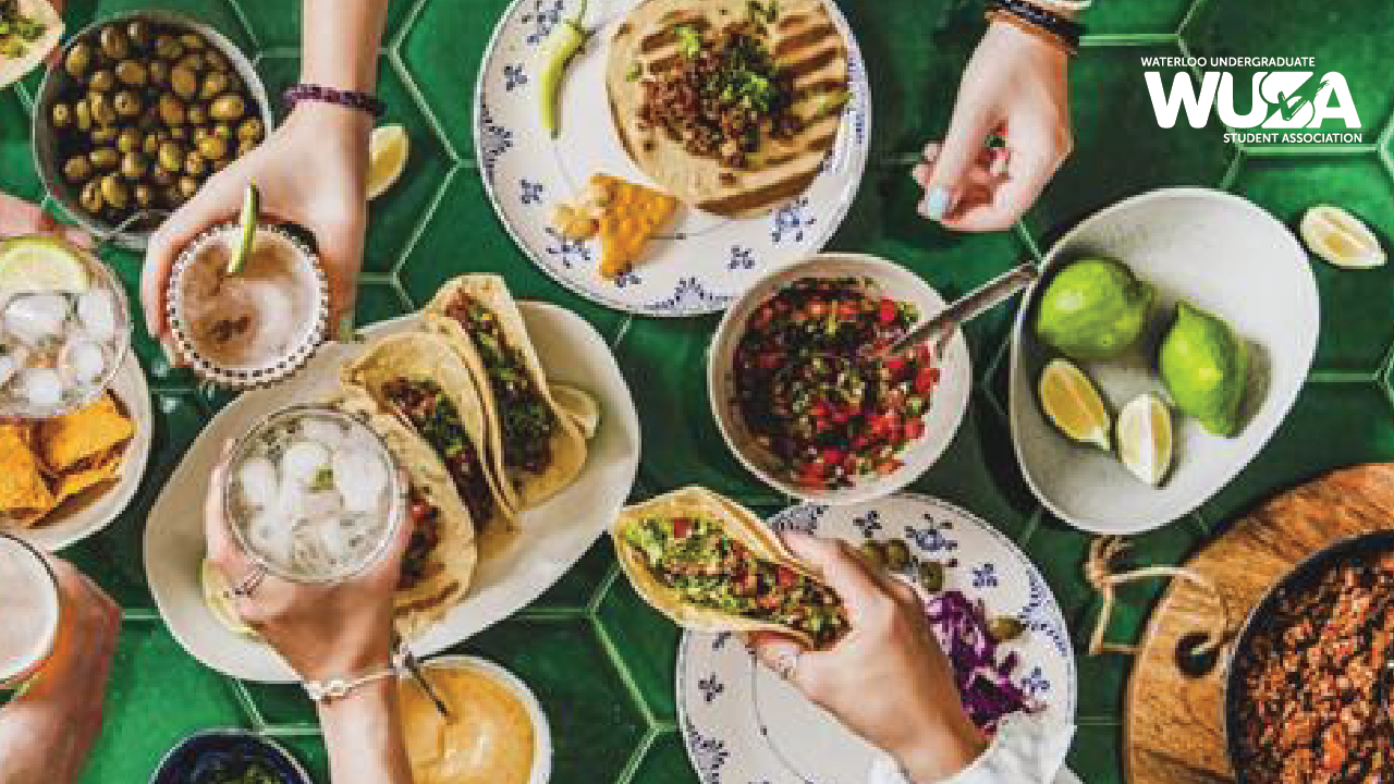 Hands eagerly reaching for Taco Tuesday delights—tacos, salsa, and drinks spread across a vibrant green table. Lime and olives add a fresh touch to the scene. Logo elegantly placed in the top right corner.