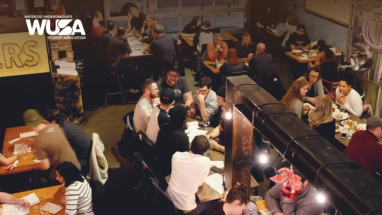 A bustling restaurant with people eating and chatting at tables, highlighted by the Waterloo Undergraduate Student Association logo, hosts a lively trivia night inspired by Abe Erb in Uptown Waterloo.